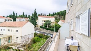 A balcony with a table and chairs, overlooking a street with buildings and greenery. - Apartments Nikola - Comfort One Bedroom Apartment With City View (Dubrovnik)