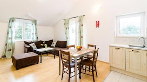 A cozy living room with a sofa, a coffee table, and a dining table with chairs. There is a kitchen area with a sink and cabinets. - Apartments Nikola - Comfort One Bedroom Apartment With City View (Dubrovnik)
