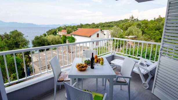 En balkon med et bord dækket til to, med udsigt over vand og grøn vegetation.