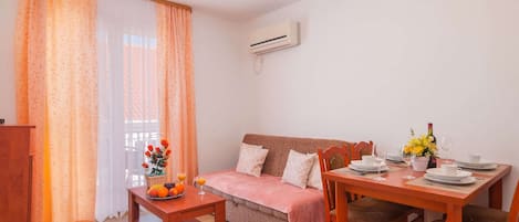 A cozy living room with a sofa, a dining table set for two, and a small side table with fruit and drinks.