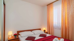 A hotel room with a single bed, two bedside tables, a nightstand, a lamp, and a window with curtains. - Apartments Island Beat - Two Bedroom Apartment With Balcony and Sea View (Supetar)