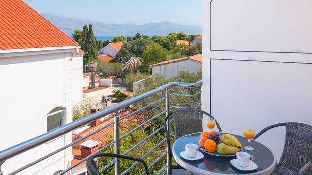 A balcony with a table set for breakfast, overlooking a scenic landscape with houses and mountains. - Apartments Island Beat - Two Bedroom Apartment With Balcony and Sea View (Supetar)