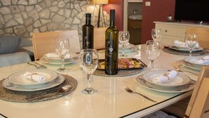 A dining table set with plates, glasses, cutlery, and wine bottles in a room with stone walls and a television in the background. - Holiday Home Luna - Two Bedroom Holiday Home With Sea View (Korcula)