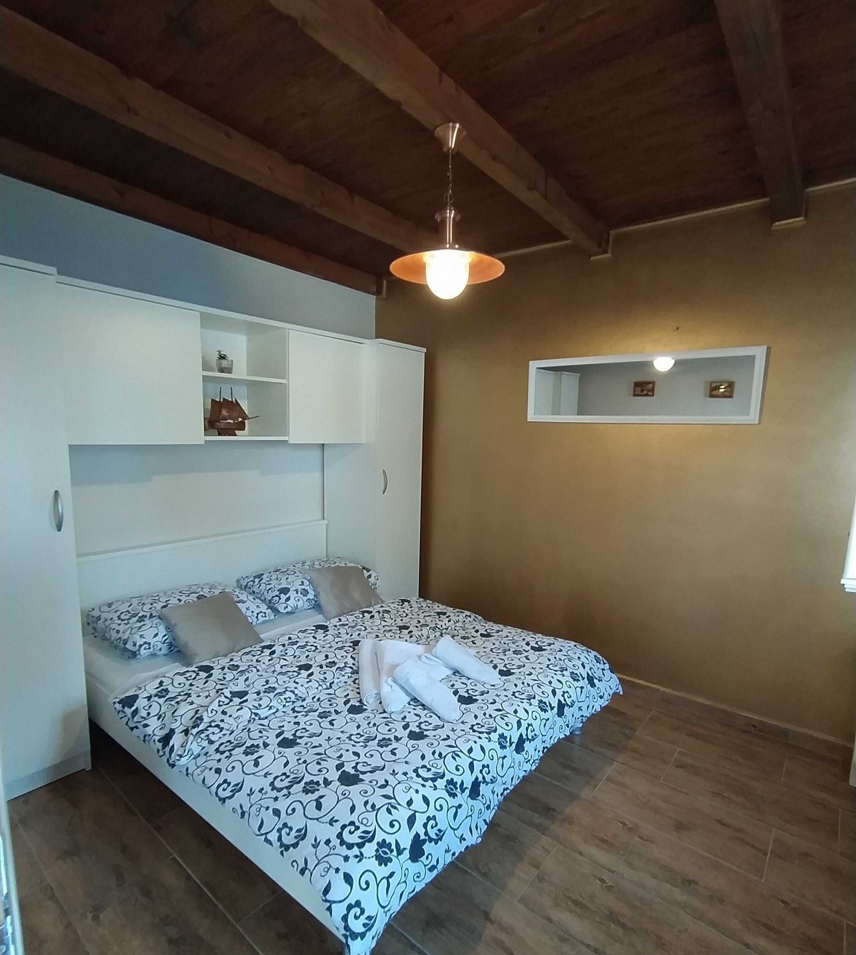 A bedroom with a bed, a wardrobe, a hanging light fixture, and a small mirror on the wall.