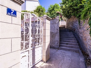 A gated entrance with a metal gate, a stone staircase, and a building with a blue sign. - Apartments Stella - One Bedroom Apartment With Terrace A2 (Dubrovnik)