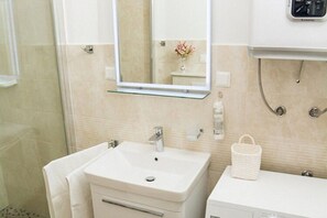 A bathroom with a white sink, a glass shelf, a mirror, a towel, and a white basket. - Apartments Stella - One Bedroom Apartment With Terrace A2 (Dubrovnik)