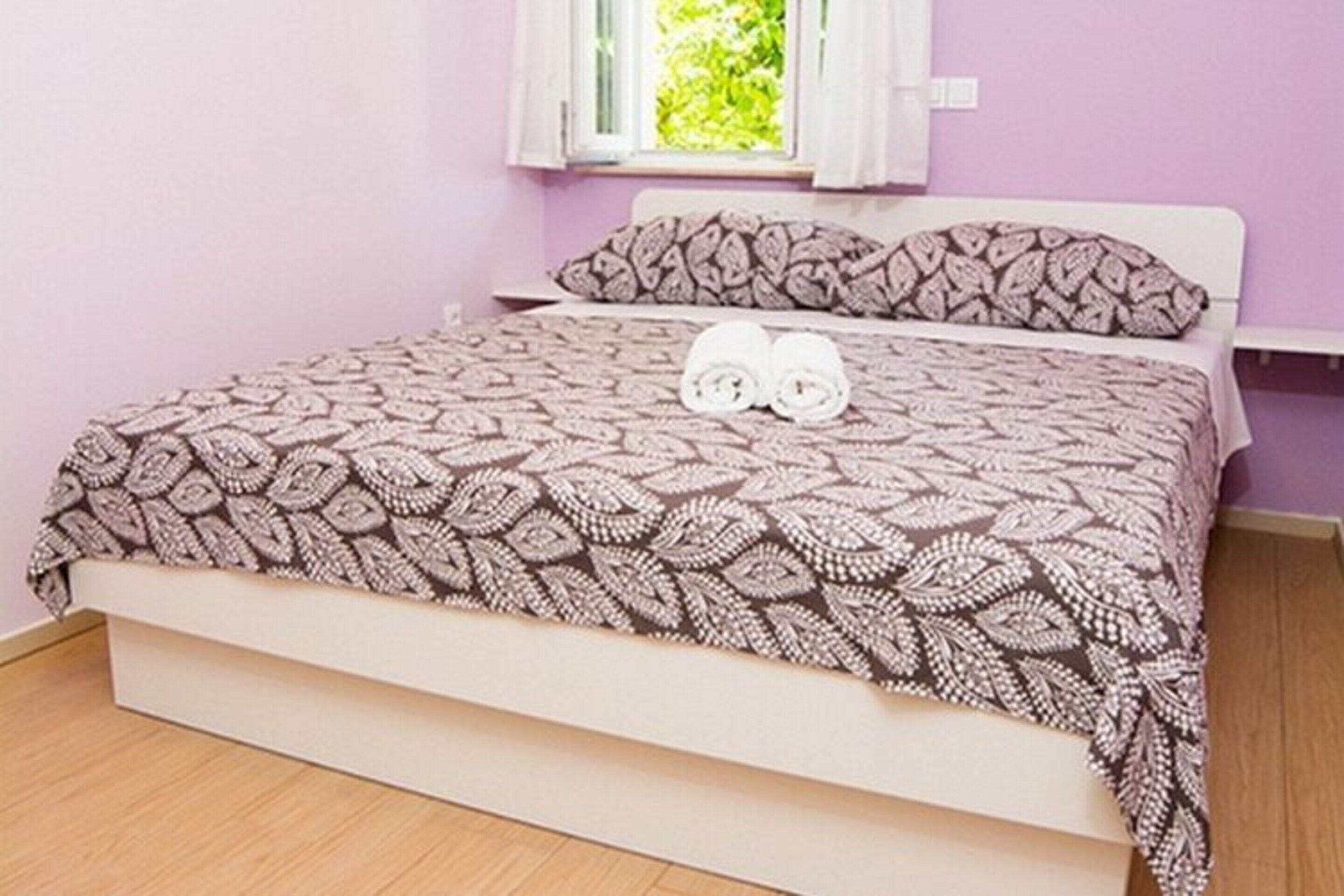 A bed with a patterned bedspread and two rolled towels on it.