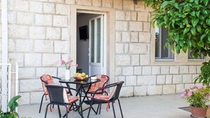An outdoor patio with a stone wall, a round table with chairs, and a potted plant. - Apartments Stella - One Bedroom Apartment With Terrace A2 (Dubrovnik)