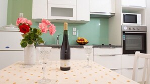A modern kitchen with white cabinets, a microwave, an oven, a wine bottle, and a vase with flowers on a table. - Apartments Stella - One Bedroom Apartment With Terrace A2 (Dubrovnik)