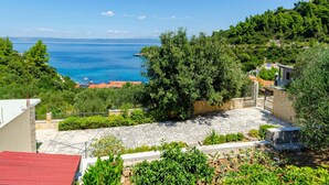 A coastal property with a stone patio, lush greenery, and a view of the sea. - Vacation House Marija, Korcula-two Bedroom Holiday Home With Terrace and Sea View (Korcula)