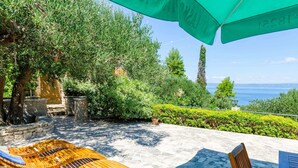 A sunlit outdoor area with wooden lounge chairs and a table, surrounded by greenery and a view of the sea. - Vacation House Marija, Korcula-two Bedroom Holiday Home With Terrace and Sea View (Korcula)