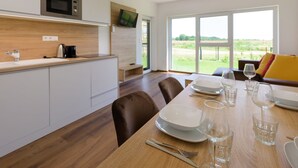 Een moderne keuken met een magnetron, spoelbak en een houten aanrecht. Er staat een eettafel gedekt met borden, glazen en bestek. De kamer heeft grote ramen met uitzicht op het omliggende landschap.