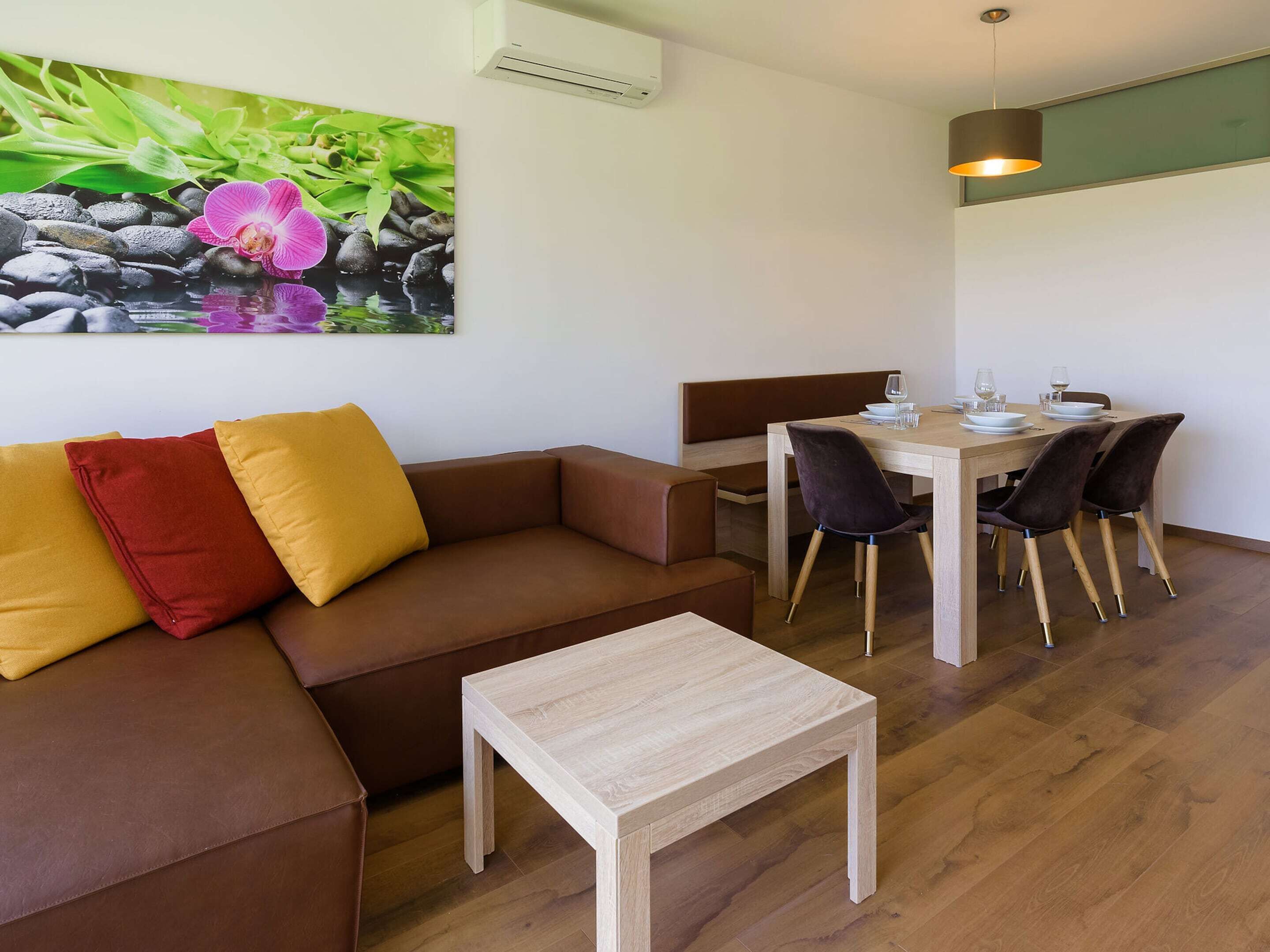 A modern living room with a brown sofa, a small wooden table, and a dining area with a wooden table and chairs.