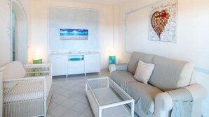 A living room with a sofa, a coffee table, a TV, and a painting on the wall. - Belvilla by OYO Monolocale Baia 8 (Golfo Aranci)