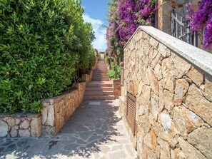 A narrow stone pathway flanked by lush green hedges and vibrant purple flowers, leading up a set of stairs. - Belvilla by OYO Monolocale Baia 8 (Golfo Aranci)