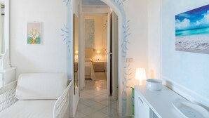 A hotel room with a bed, a nightstand, a lamp, and a view of the beach through the window. - Belvilla by OYO Monolocale Baia 8 (Golfo Aranci)