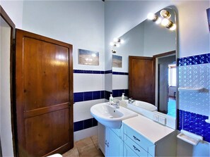 A bathroom with a white sink, blue and white tiled walls, a wooden door, and a mirror with lights. - Holiday Home in Assisi With Garden (Assisi)