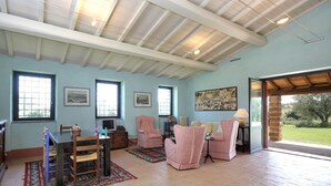 Ein geräumiges Wohnzimmer mit hoher Decke, großen Fenstern und Blick ins Freie.