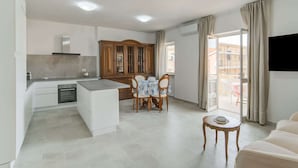 A modern kitchen with a dining area, a sofa, and a TV mounted on the wall. - Apartment in Sardegna Near Beach (Arzachena)