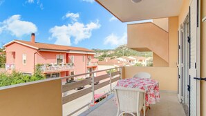 A balcony with a table and chairs, overlooking a pink building and a hillside. - Apartment in Sardegna Near Beach (Arzachena)