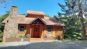 A log cabin with a stone chimney, a red door, and a small porch area. - Cozy ski  retreat, close to Appalachian ski mountain in blowing rock and boone  (Blowing Rock)