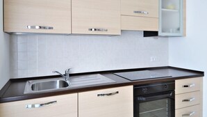 A modern kitchen with light wood cabinets, a stainless steel sink, a black oven, and a glass-fronted cabinet. - Apartment by Lake Como With Scenic Views (Dervio)