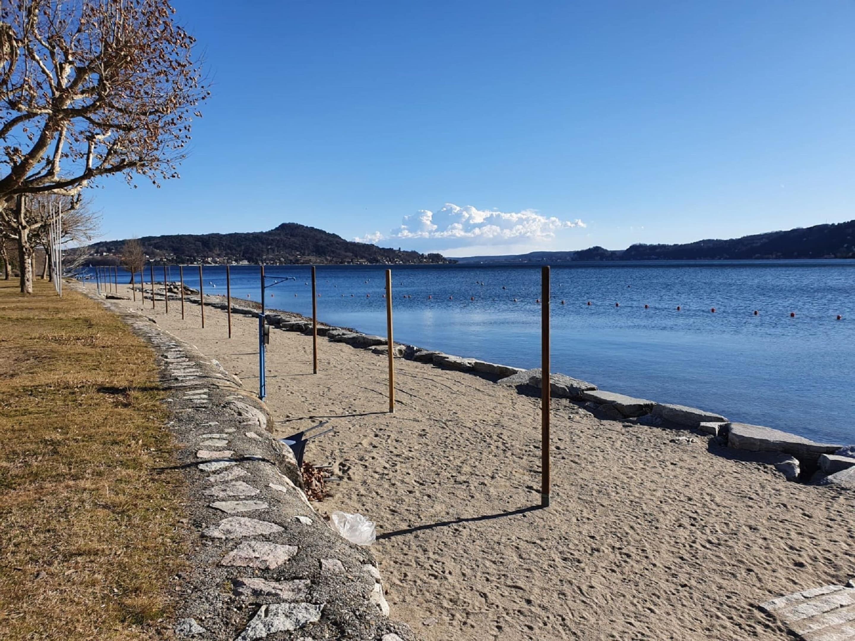A beach with a stone pathway, a row of poles, and a clear view of the water and distant hills.