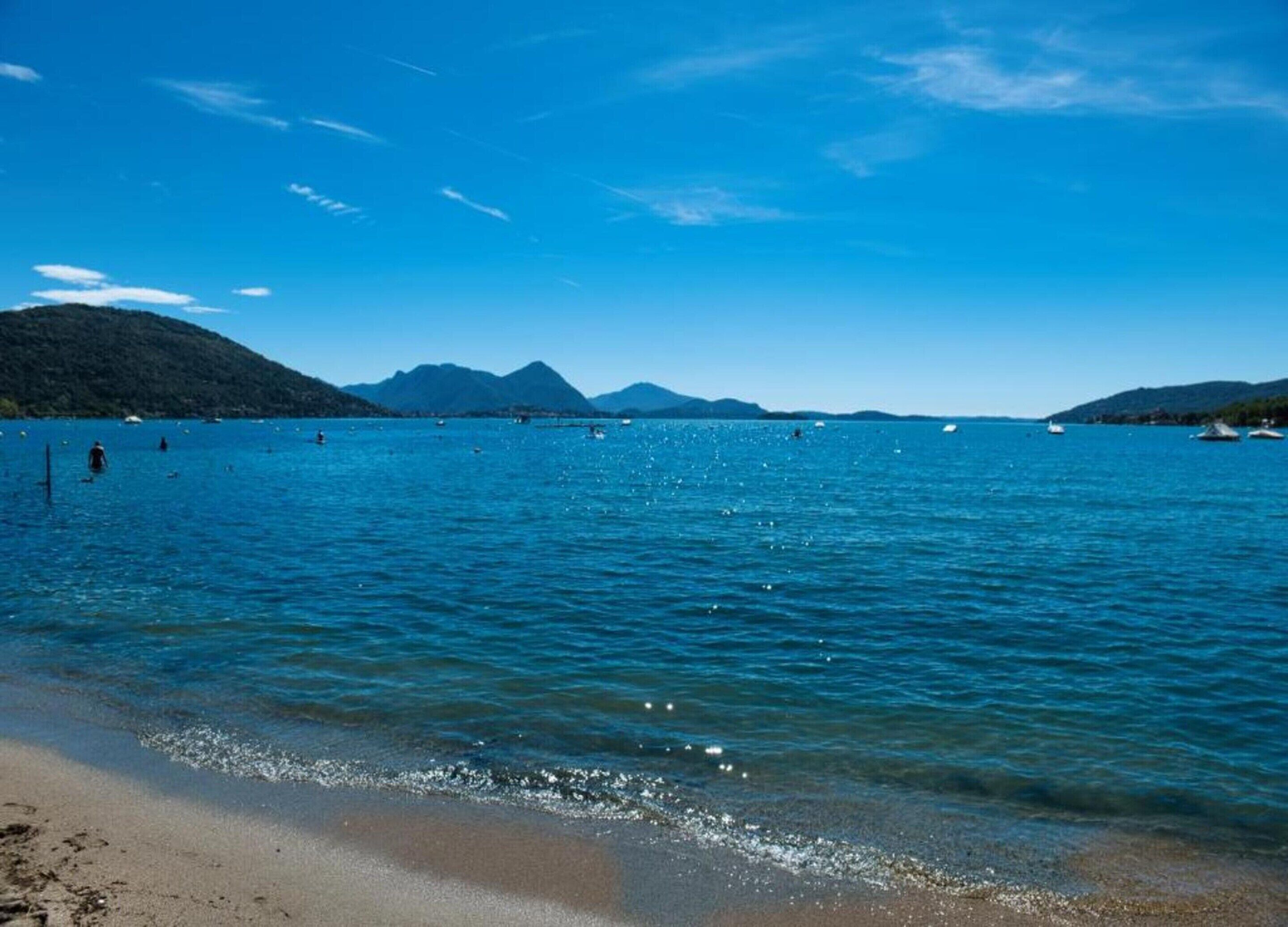 A beach with clear blue water, boats, and mountains in the background.