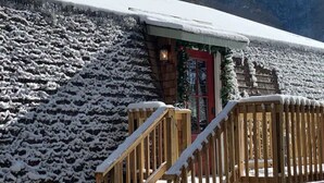 A snow-covered stone building with a red door, wooden staircase, and a small porch. - The Owl Barn - Most Unique Cabin in The Smokies. Hot Tub, Family & Pet Friendly (Sevierville)