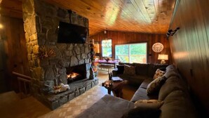 A cozy living room with a stone fireplace, wooden ceiling, and a comfortable couch. - The Owl Barn - Most Unique Cabin in The Smokies. Hot Tub, Family & Pet Friendly (Sevierville)