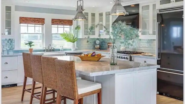 Une cuisine moderne avec des meubles blancs, un îlot central doté de tabourets, des luminaires suspendus et un grand réfrigérateur.