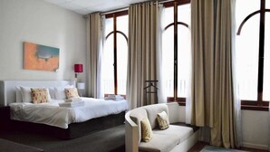 A hotel room with a bed, a sofa, a window with curtains, a painting on the wall, and a lamp. - 1 Bedroom Apartment With Roof Top Views (Cape Town)