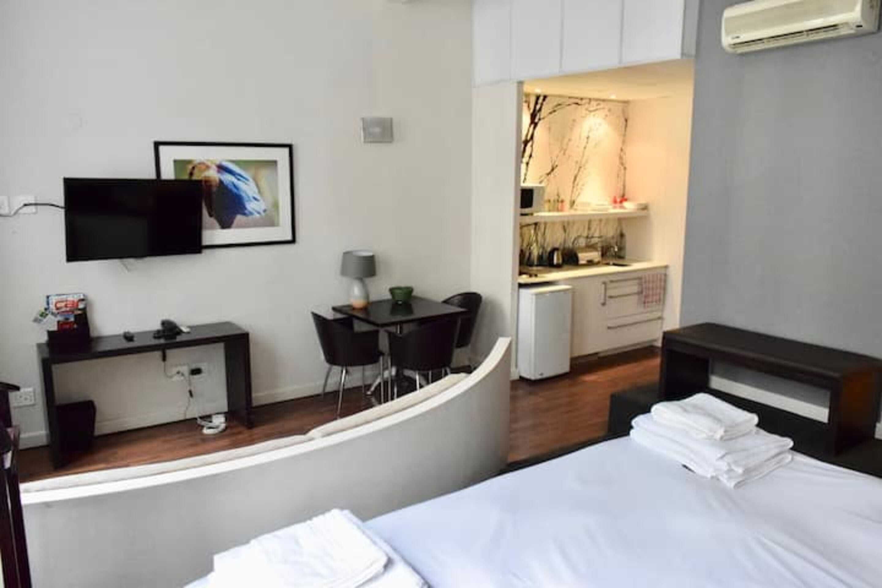 A hotel room with a bed, a desk, a chair, a TV, and a small kitchenette.