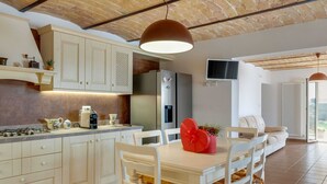 A modern kitchen with a central island, white cabinetry, and a dining area with a table and chairs. - Belvilla by OYO Villa Intera 12 Pax (Collecorvino)