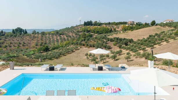 A swimming pool with lounge chairs and umbrellas, surrounded by olive groves and a hilly landscape. - Belvilla by OYO Villa Intera 12 Pax (Collecorvino)