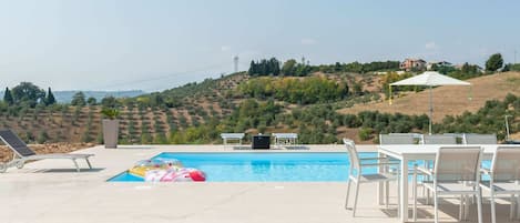 A swimming pool with lounge chairs and a table, surrounded by a stone deck.