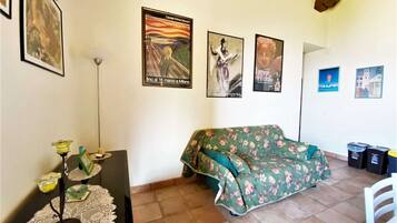 Una stanza con un divano floreale, un tavolino con tovaglia in pizzo e diverse opere d'arte appese alle pareti.