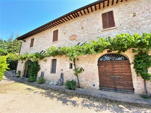 A stone building with a rustic appearance, featuring a large wooden door and multiple windows with shutters. - Holiday Home in Assisi With Garden Views (Assisi)