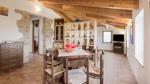 A rustic dining area with a wooden table and chairs, a stone wall, and a wooden cabinet with glass doors. - Belvilla by OYO Bilocale 2adeg Piano (Assisi)