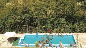 A swimming pool with lounge chairs and a small deck area, surrounded by dense forest. - Belvilla by OYO Bilocale 2adeg Piano (Assisi)