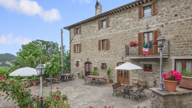 A stone building with outdoor seating, potted plants, and a flag. - Belvilla by OYO Bilocale 2adeg Piano (Assisi)