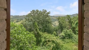 A view through a window with a stone wall, overlooking a lush green landscape with trees and hills. - Belvilla by OYO Bilocale 2adeg Piano (Assisi)