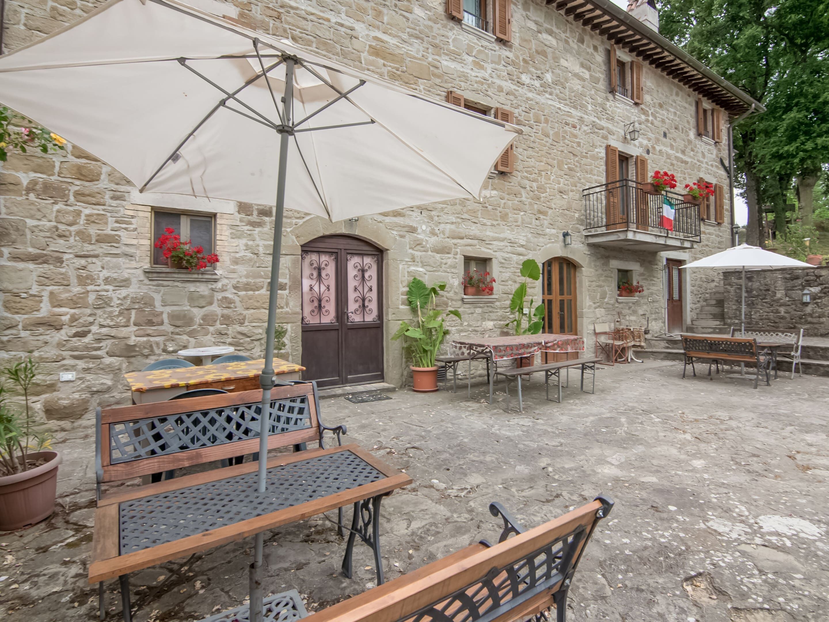 An outdoor seating area with tables and benches, surrounded by stone buildings with windows and balconies.