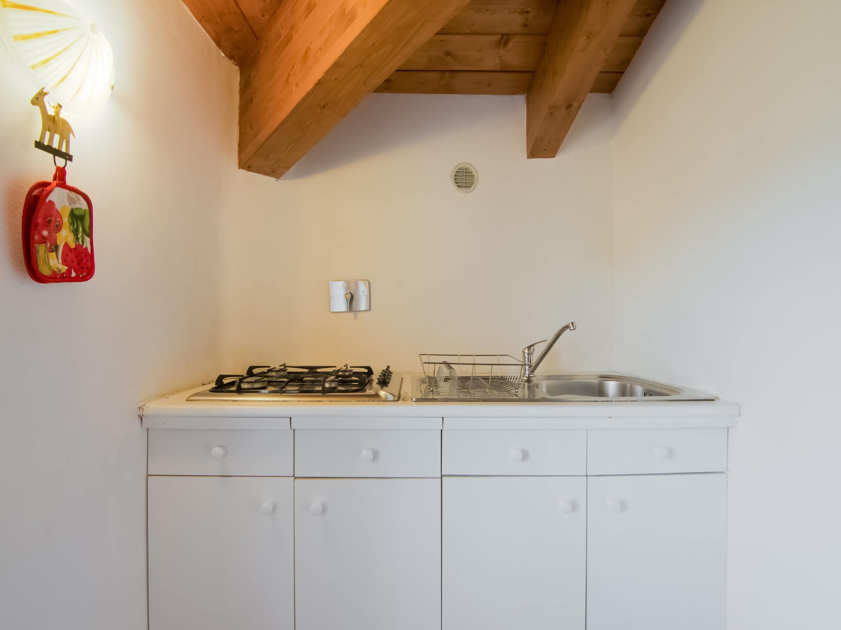 Eine kleine Küche mit Gasherd, Spüle und einem weißen Schrank mit Schubladen.