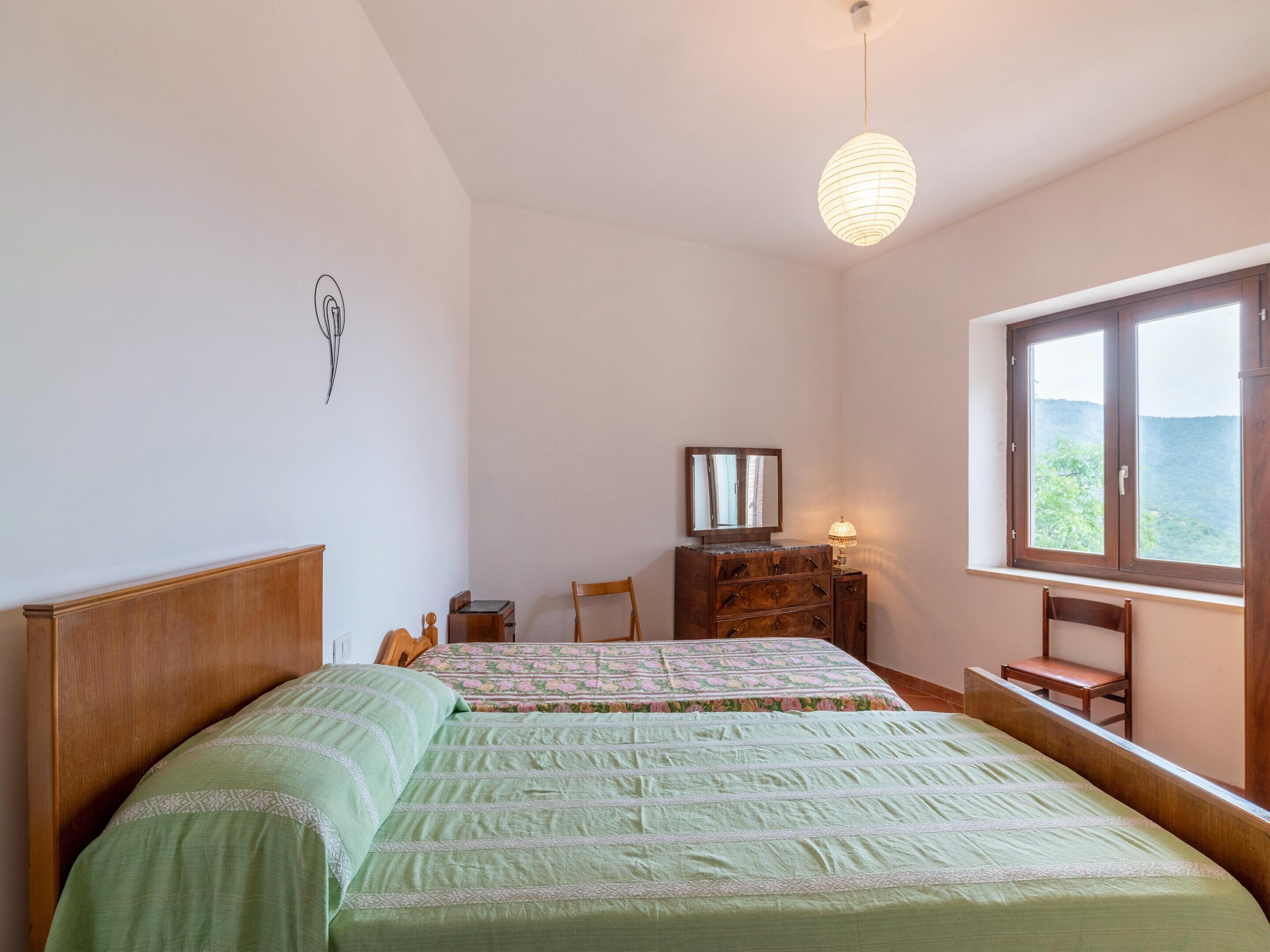 A bedroom with two beds, a dresser, a chair, a lamp, and a window with a view.