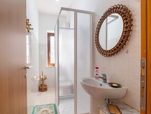 A bathroom with a glass shower door, a white sink with a soap dish, and a wicker-framed mirror. - Belvilla by OYO Casa Polino (Polino)