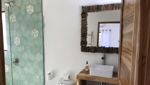 A bathroom with a glass shower, a toilet, a sink, and a mirror. - Honeymoon apt with mini fridge and pool view (Playa junquillal)