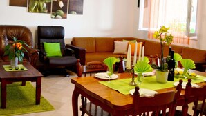 A living room with a brown leather sofa, a dining table with chairs, and a window with orange curtains. - Apartments Lina - Two Bedroom Apartment With Terrace (Dubrovnik)
