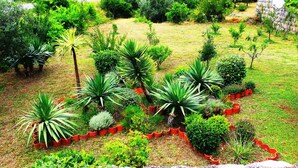 A landscaped garden with various plants and trees, surrounded by a stone wall and a hillside in the background. - Apartments Lina - Two Bedroom Apartment With Terrace (Dubrovnik)