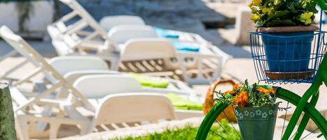 A poolside area with lounge chairs and a bicycle with a basket of flowers.